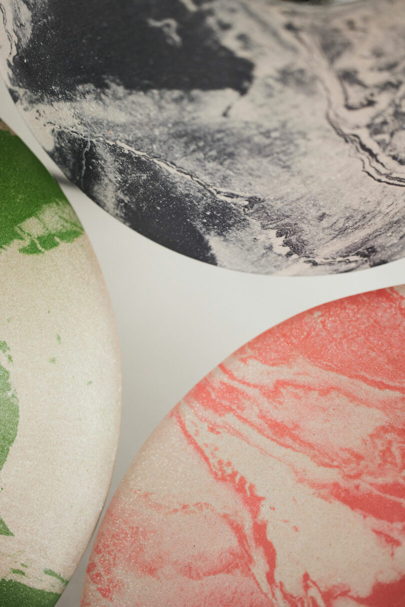 Three round Upglas surfaces designed by Luca Nichetto feature marbled patterns in black and white, green and white, and pink and white, partially overlapping on a clean white background.