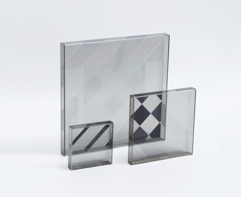 Three transparent, square glass panels with etched geometric patterns are standing upright against a plain white background