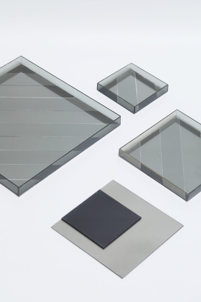Four rectangular and square glass or acrylic sheets, some tinted and one dark, are arranged on a plain white background