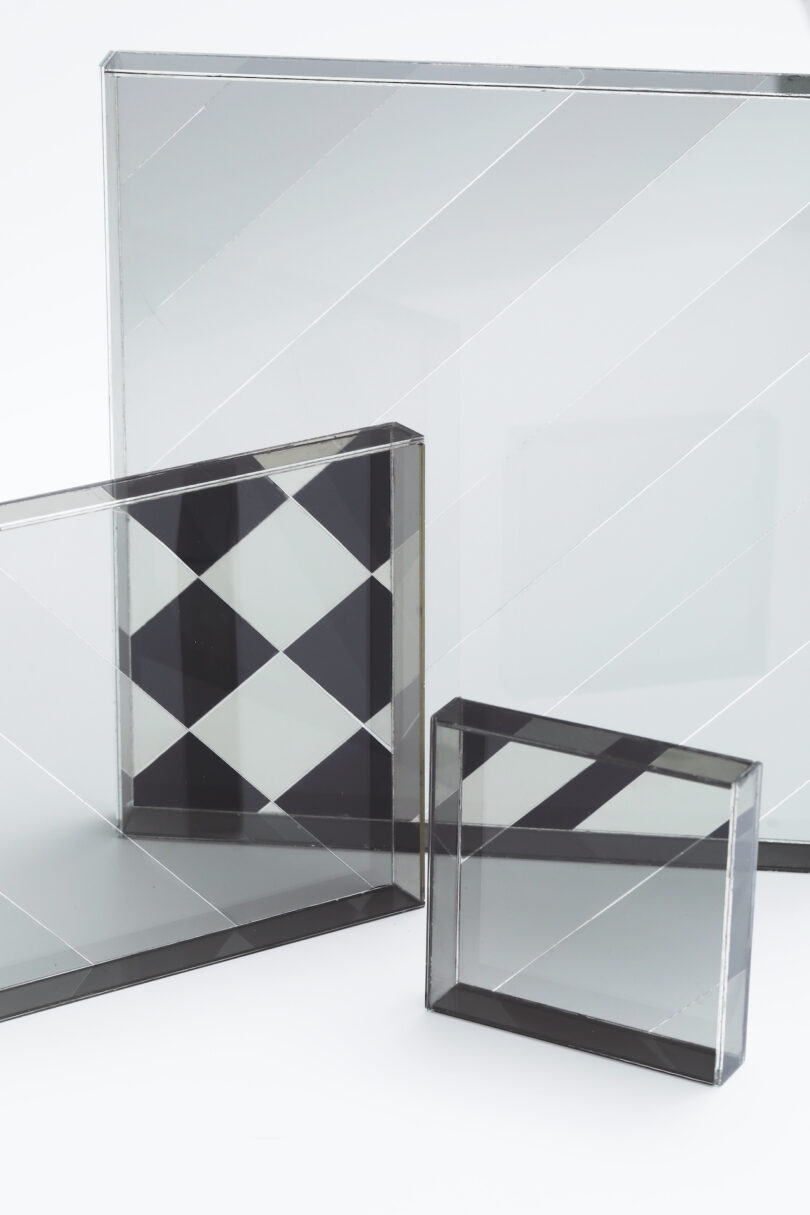 Three rectangular glass blocks with geometric patterns and diagonal lines are arranged on a white surface