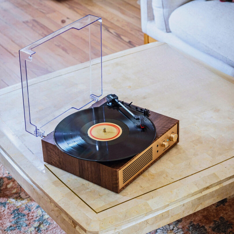 A vintage-style Crosley Miles record player with a clear dust cover is placed on a wooden shelf with a curved frame.