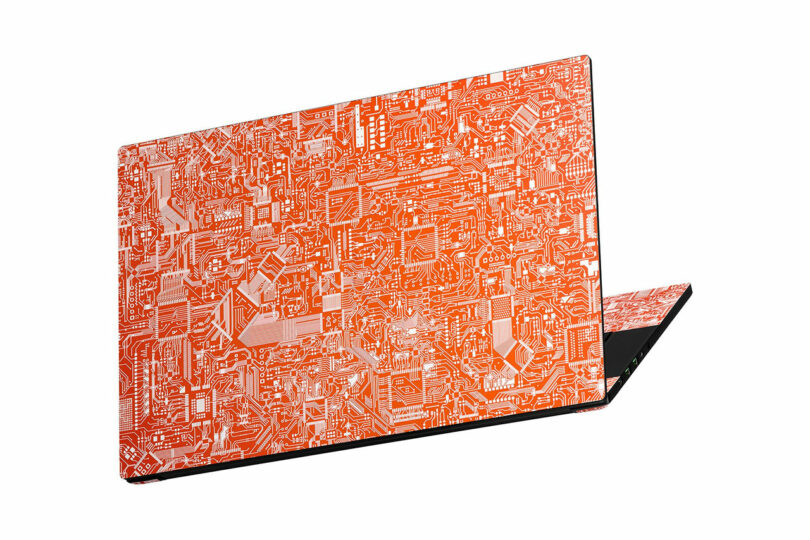 A closed laptop with a Dbrand orange and white circuit board pattern on the lid and top edge, shown on a white background.