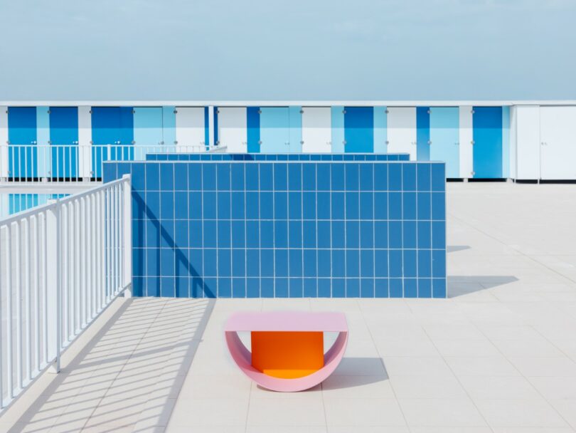 A pink and orange bench sits on a tiled rooftop terrace with a blue tiled wall and blue and white lockers in the background