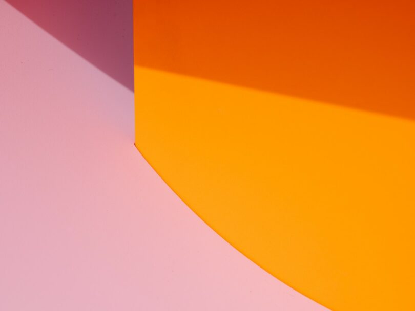 Abstract image featuring a curved pink surface meeting an orange wall with a shadow, creating a geometric pattern with contrasting colors