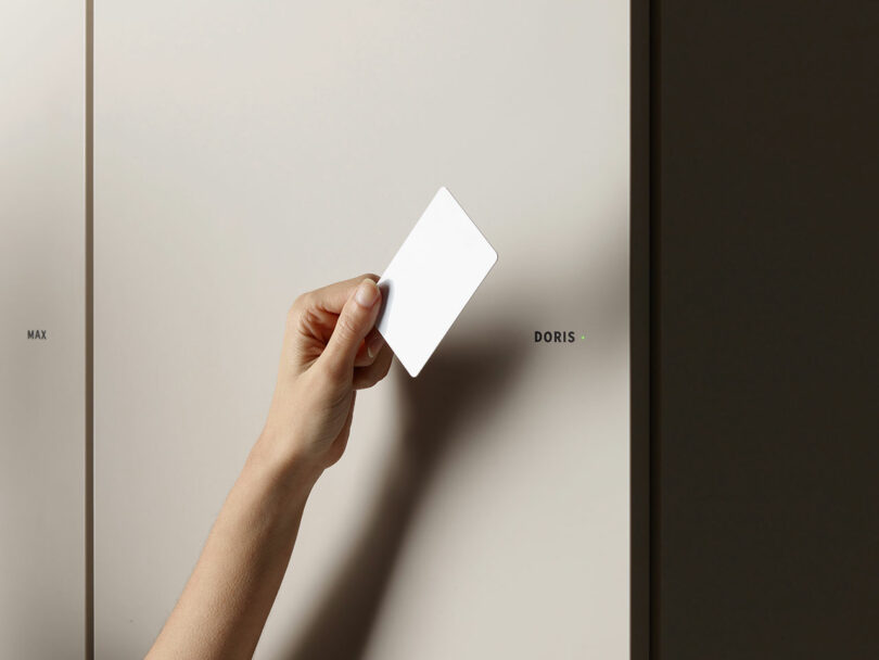 A hand holding a white card in front of a locker labeled "DORIS" with a small green light next to the label.