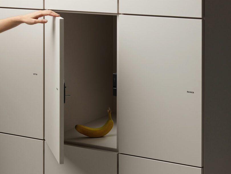 A hand opens a white locker door to reveal a single banana inside the otherwise empty locker.