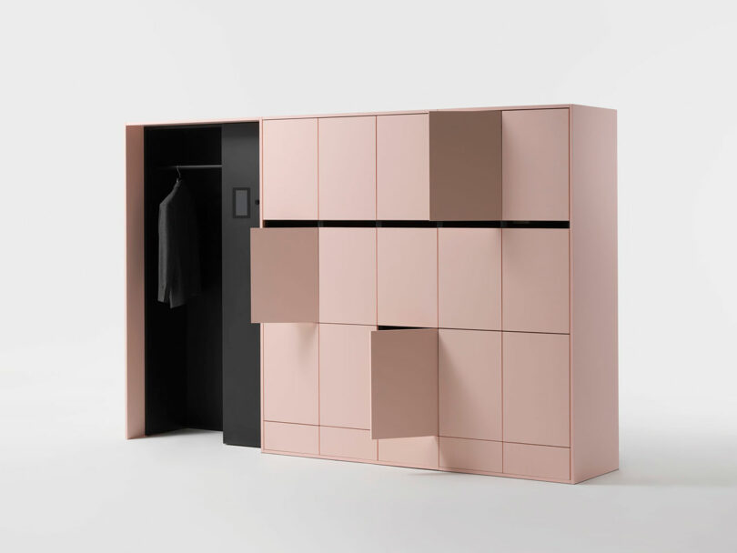A minimalist wardrobe with a matte pink finish, several doors partially open, and a section showing a black interior with a single jacket hanging.