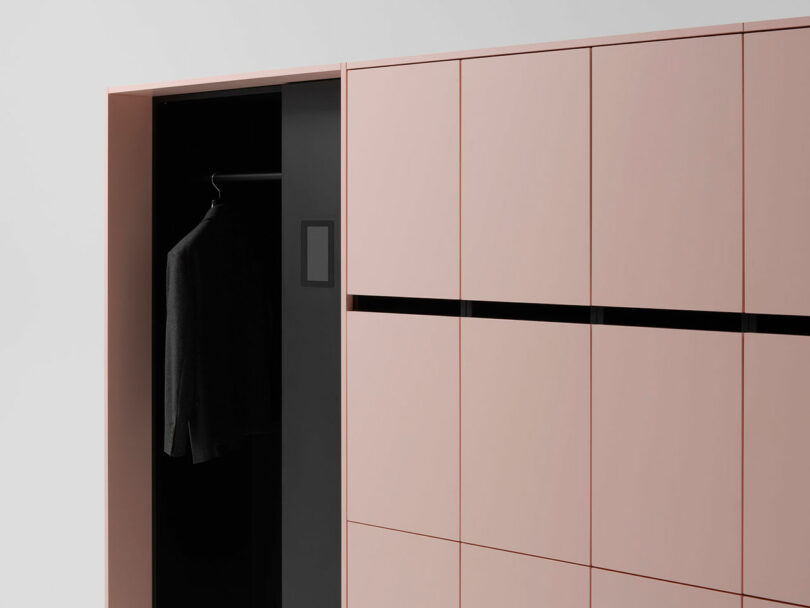 Minimalist wardrobe with pink cabinet doors, one open section showing a single black coat on a hanger inside a black interior compartment.