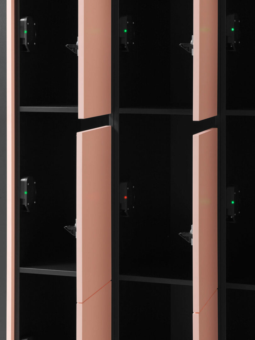 A close-up view of several open lockers with pink doors and black interiors, showing individual shelves and small indicator lights inside each compartment.