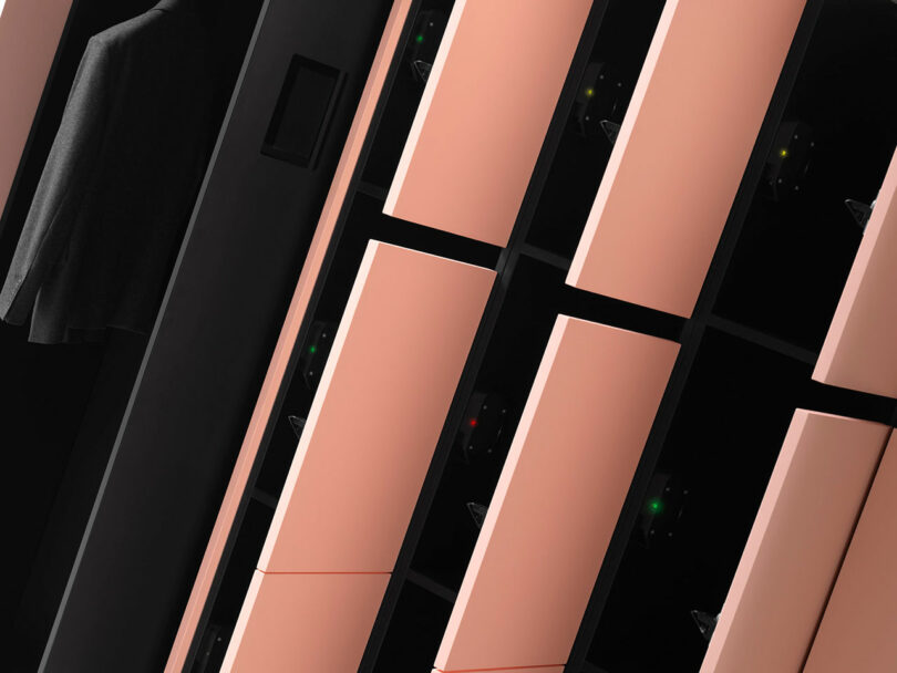 Close-up view of angled, modern lockers with pink doors and dark trim; one locker is slightly open revealing a hanging garment.