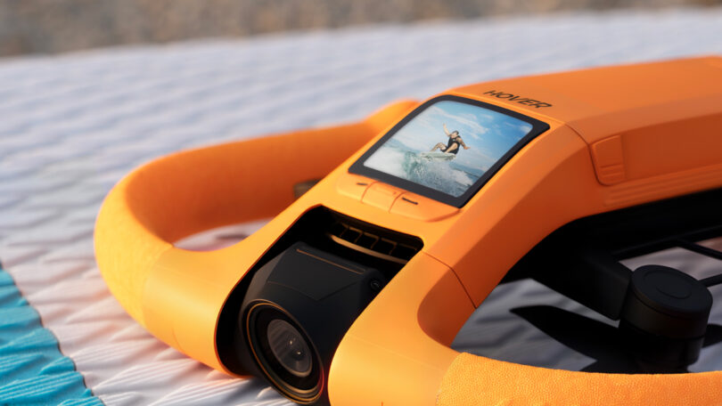 A large plan of orange waterproof devices with a screen showing a person surfing; The device rests on a textured white surface.