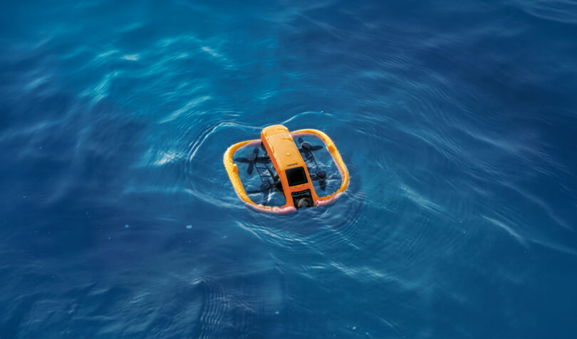 The yellow underwater drone with protective bumpers floats on the surface of clear blue water.