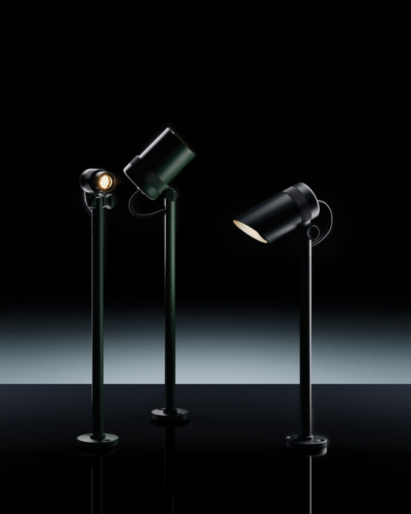 Three modern black spotlights on tall stands are displayed against a dark gradient background, each angled in different directions