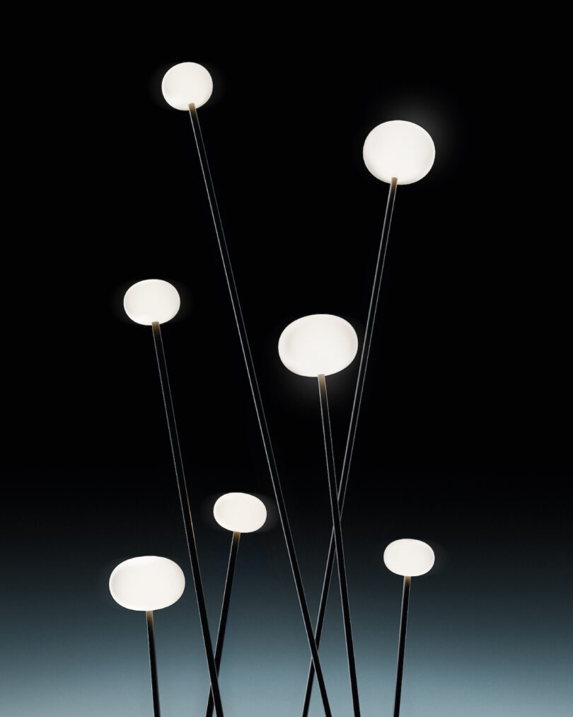 Seven modern outdoor lights with spherical white bulbs on thin black stands arranged at varying heights against a dark gradient background.