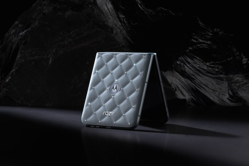 A Motorola Razr flip phone with a quilted-texture cover is partially open, displayed against a dark, rocky background.