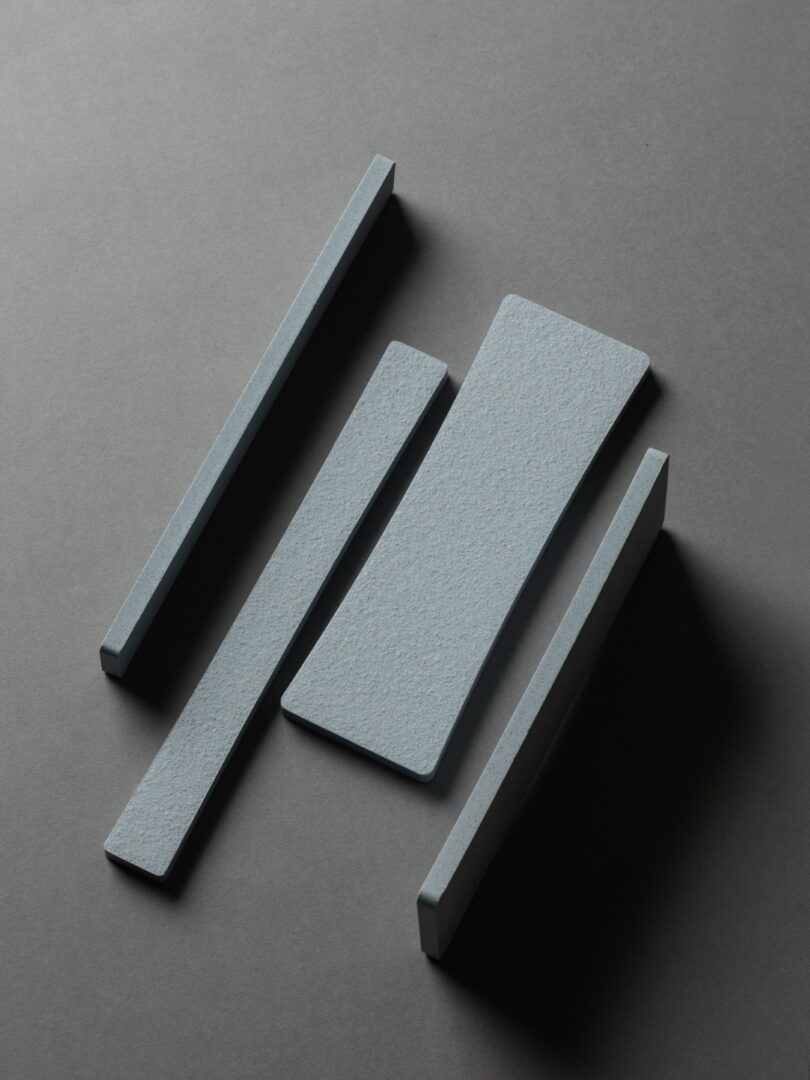 Cuatro mosaicos rectangulares grises están dispuestos sobre una superficie gris oscuro, con tres mosaicos delgados paralelos y un mosaico más ancho y en ángulo en el medio.