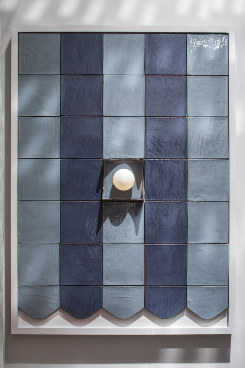 A grid of blue ceramic tiles with a central recessed tile holding a white spherical light, framed by a white border.