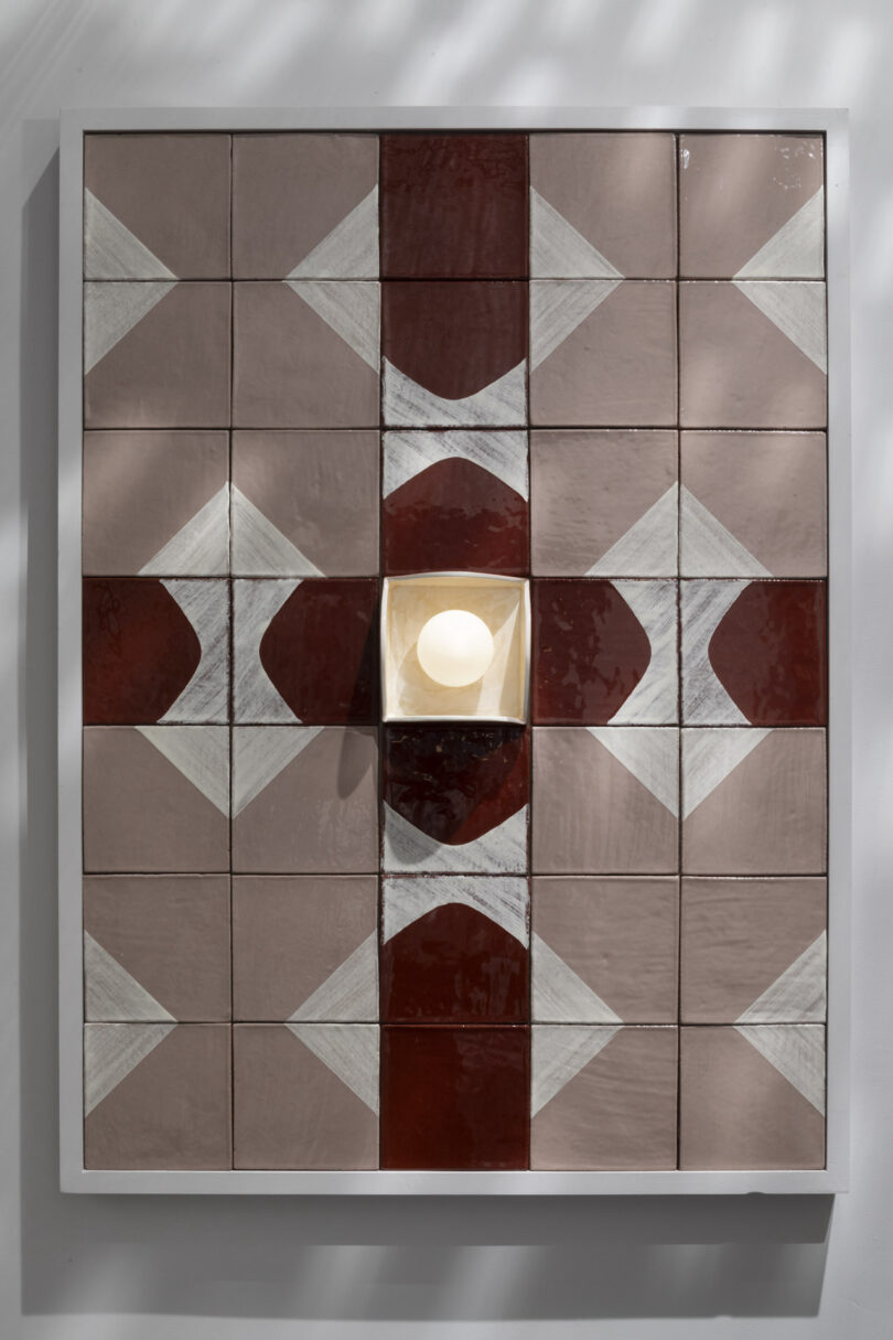 A geometric wall art piece made of square pink, white, and red tiles forms a symmetrical pattern with a central light fixture