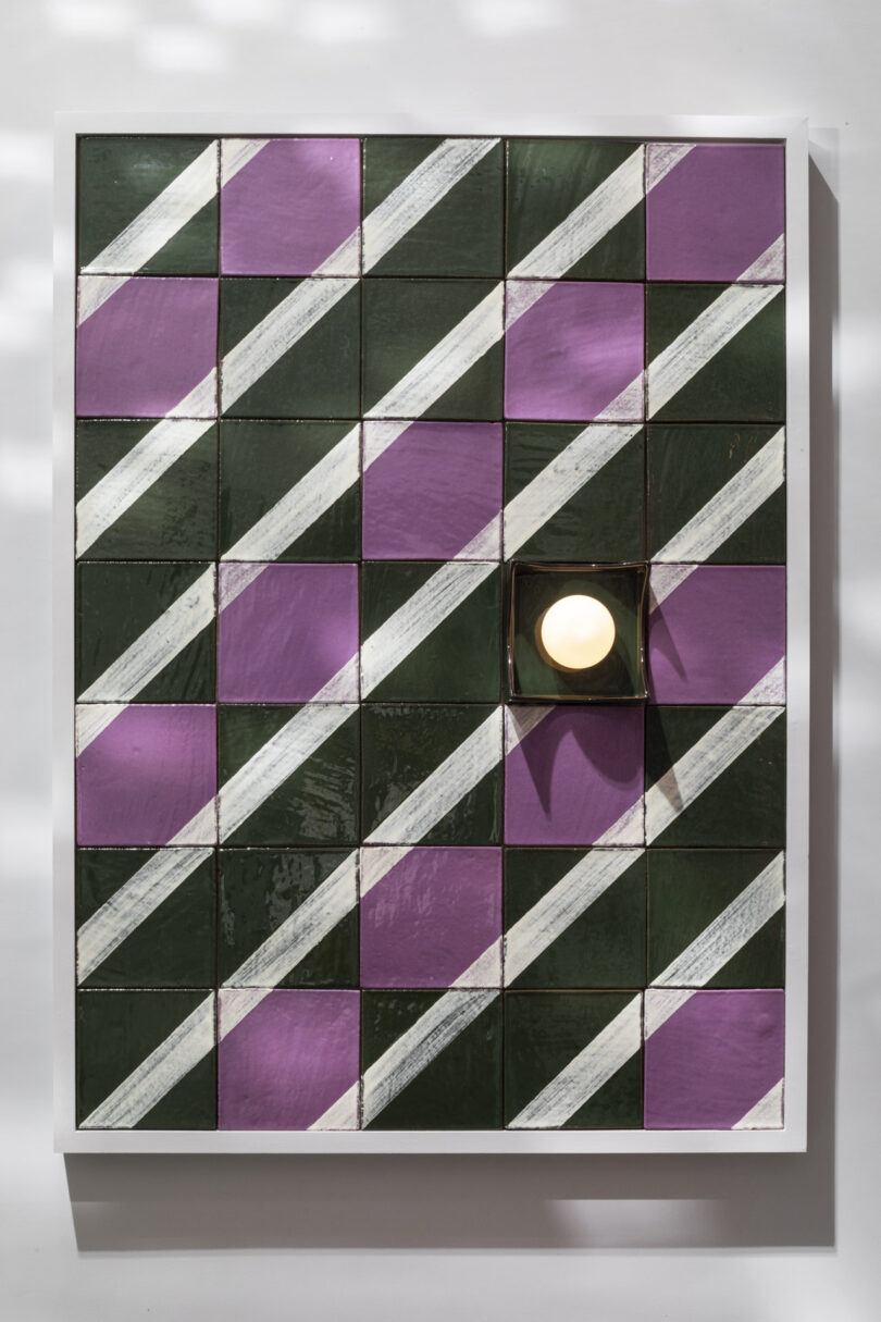 Rectangular grid artwork with alternating pink, dark green, and white diagonal-striped tiles; one tile is replaced by a round, lit bulb in the lower right area