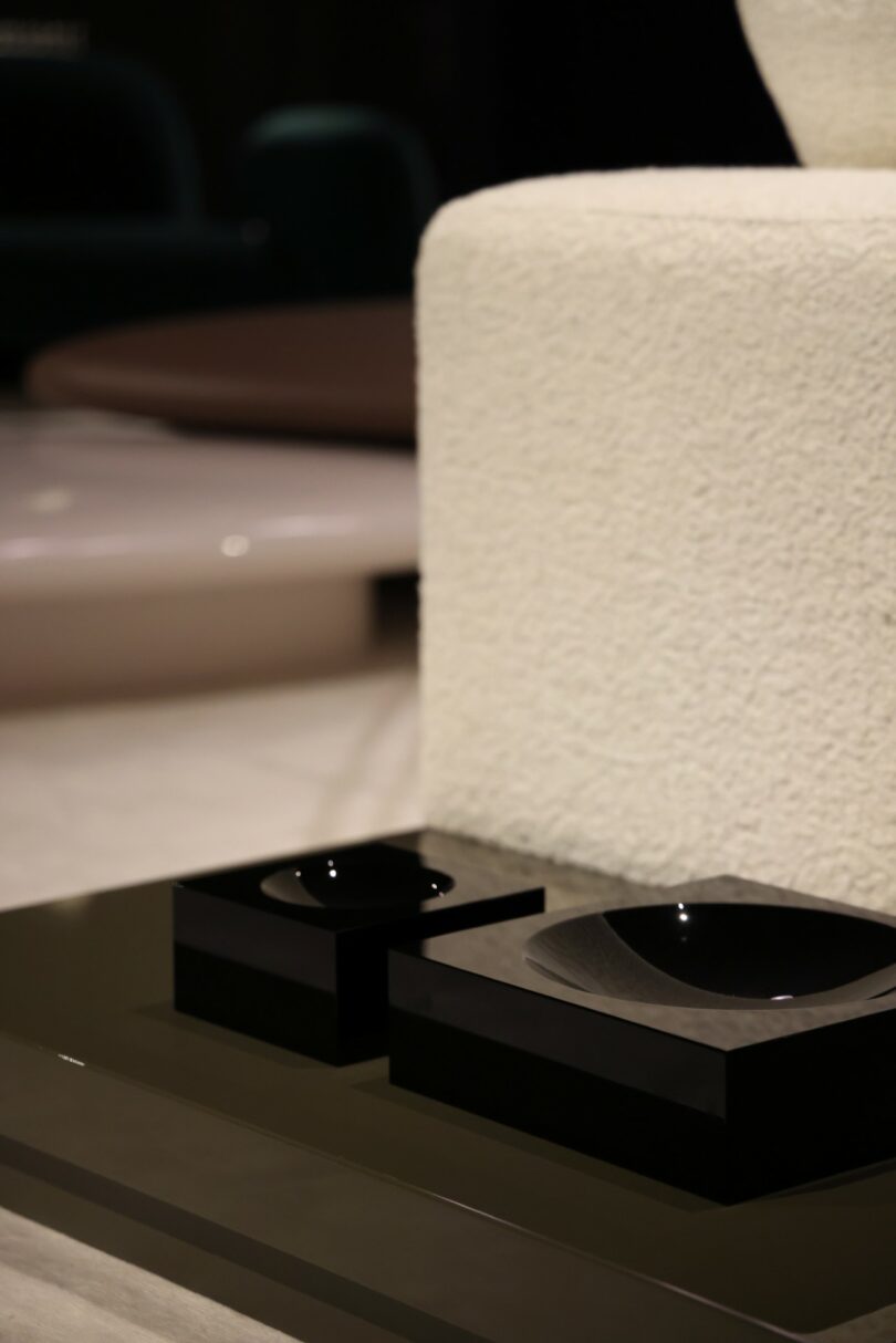 Close-up of a modern, minimalist interior with a textured white chair, glossy black square objects, and a sleek dark surface