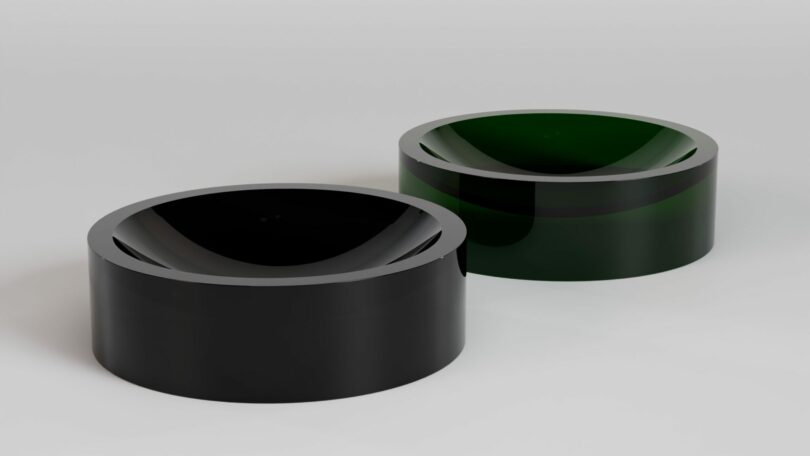 Two round, glossy, hollow cylinders—one black and one dark green—sit side by side on a plain white surface