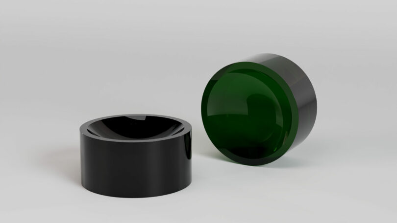 Two black cylindrical objects are placed on a plain light surface; one is upright and the other is lying on its side, showing a green-tinted interior