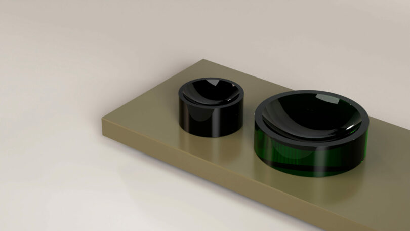A rectangular metallic surface with two glossy, cylindrical buttons—one small and black, one large and dark green—positioned on the right side