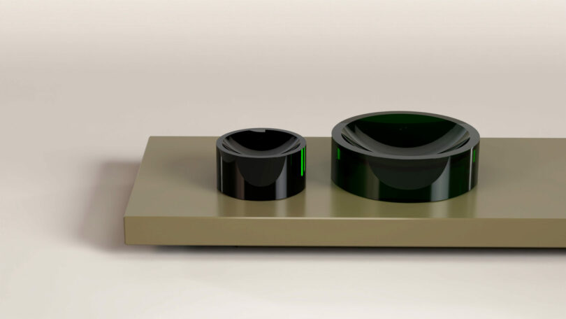 Two black cylindrical objects, one larger than the other, rest on a flat rectangular beige platform against a plain background