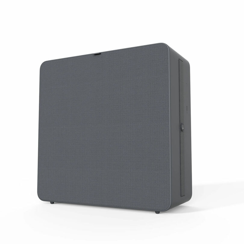 A rectangular gray speaker or electronic device with a fabric front and a minimalist design, photographed on a white background.