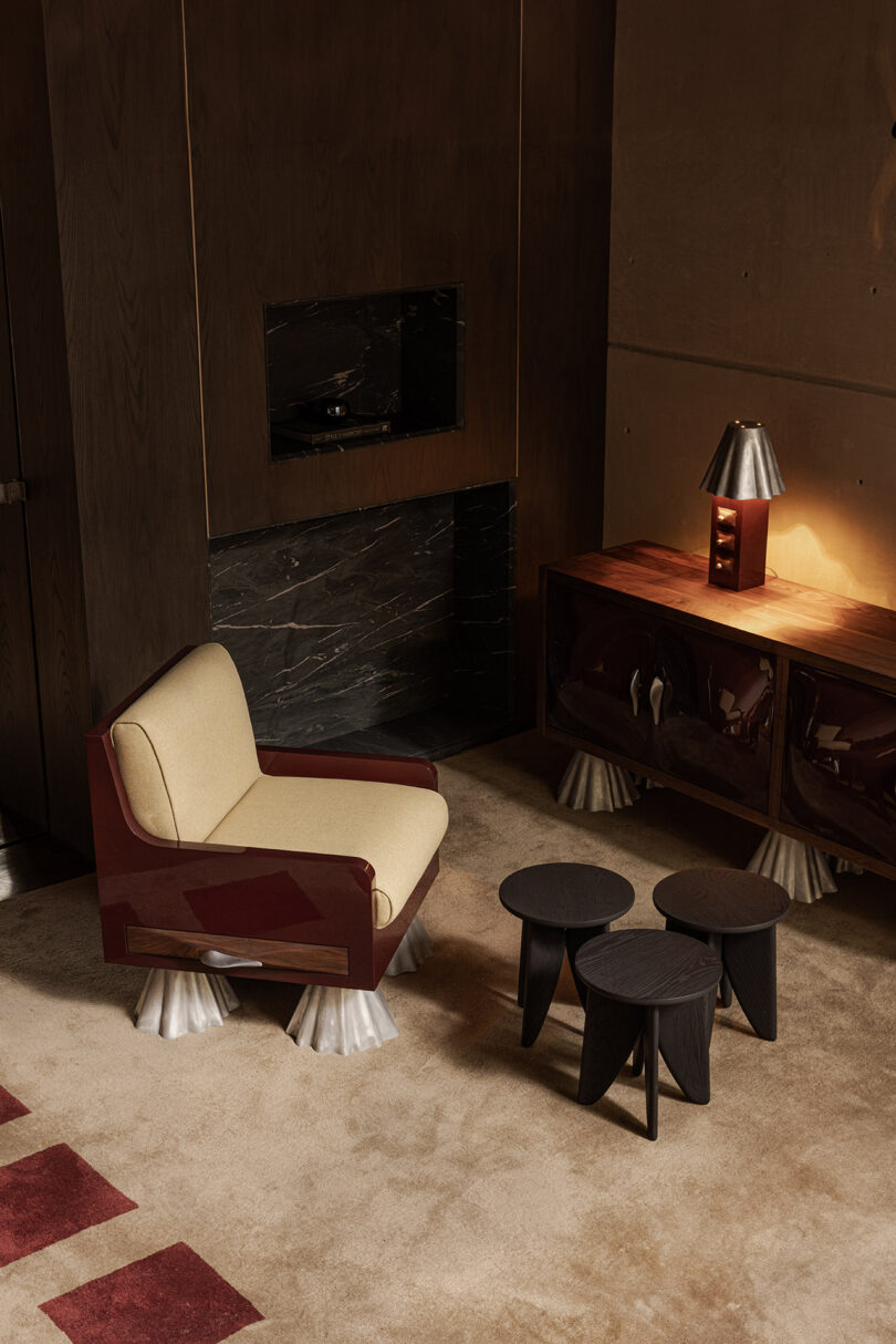 A modern living room with a beige armchair, three black coffee tables, a wooden cabinet with a lamp, and a marble fireplace, all set on a beige carpet.