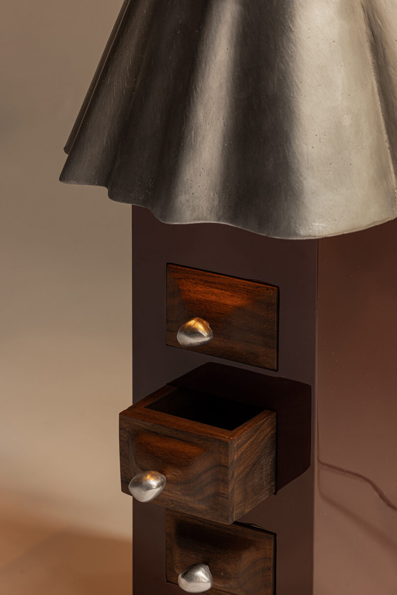 A close-up of a brown cabinet with a metallic top and three wooden drawers—one open—each featuring silver handles.