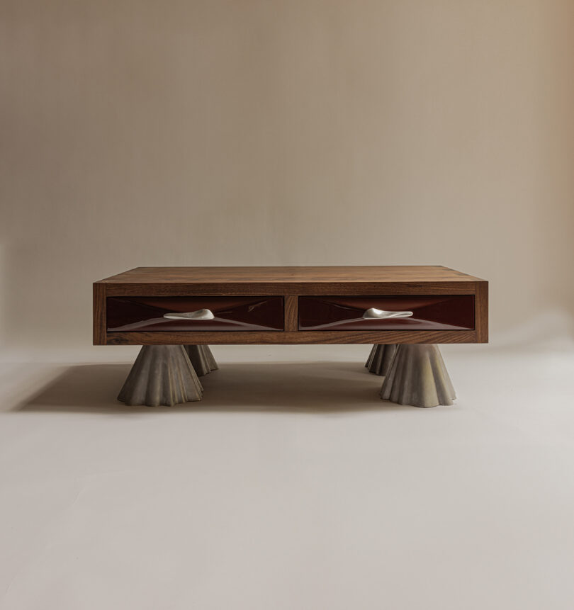 A rectangular wooden coffee table with two drawers and four sculptural, cone-shaped metallic legs on a plain neutral background.