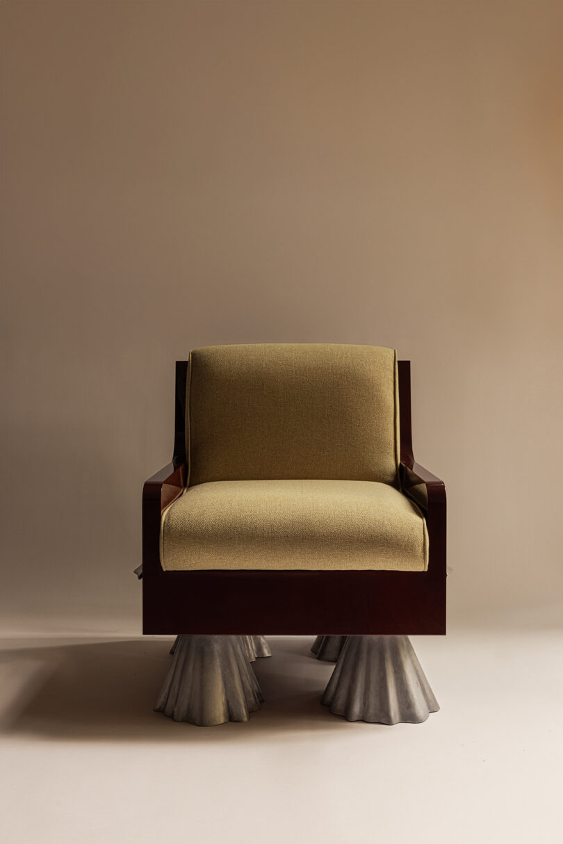 A modern armchair with olive upholstery, dark wooden frame, and four sculptural, metallic cone-shaped legs flair against a neutral background.