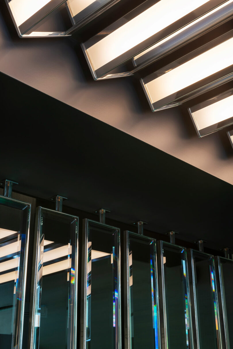 Rectangular ceiling lights with mirrored panels below reflect light, creating geometric patterns in a modern interior.