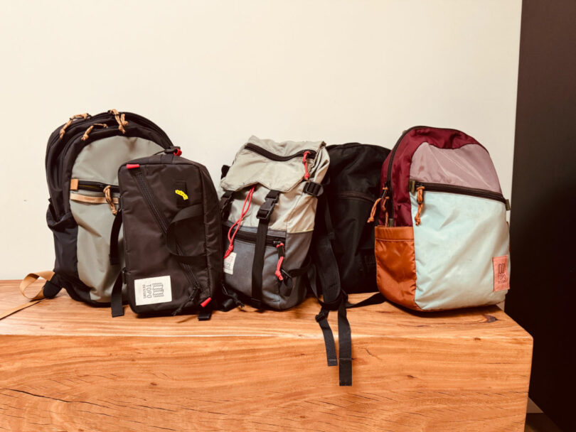 Cuatro mochilas de diferentes colores y estilos se colocan uno al lado del otro en una superficie de madera contra un fondo liso.