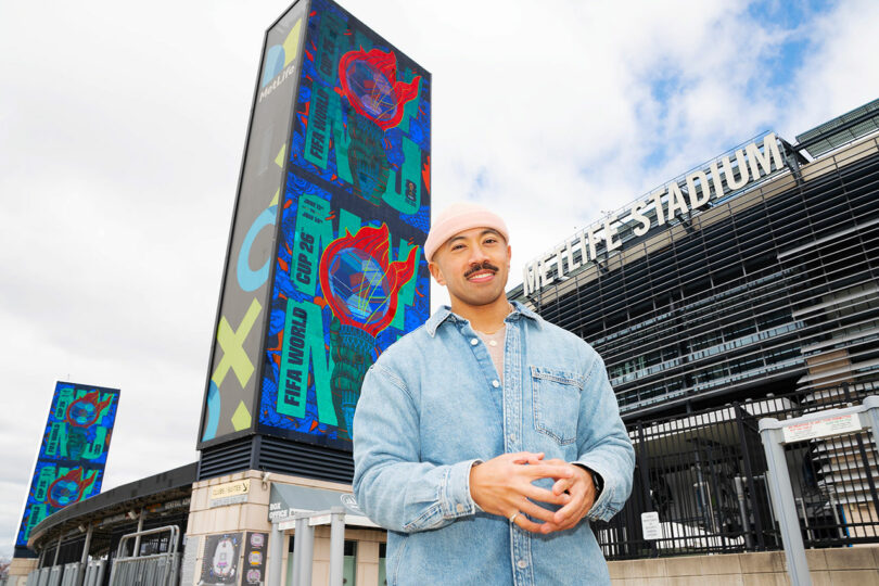 The person in the grass shirt stands in front of the MetLife Stadium, with colorful digital FIFA World Cup 26 Banners that are displayed outside.