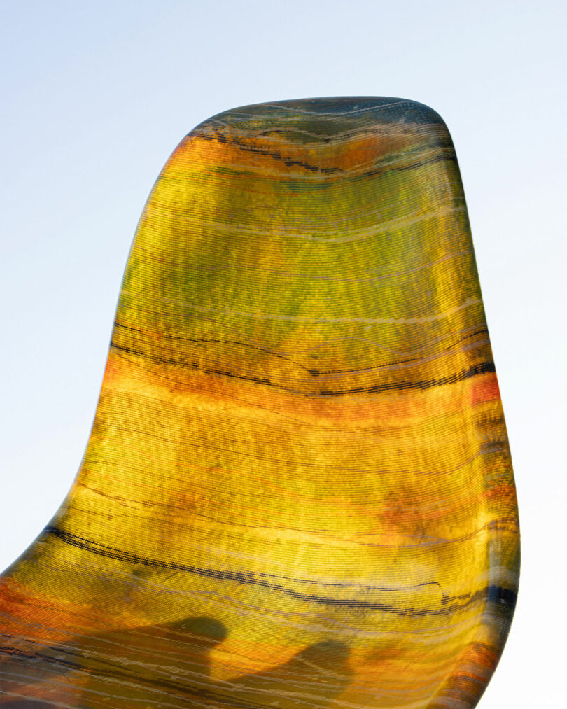 A close-up of a modern chair with a yellow and orange marbled texture, set against a plain blue background.