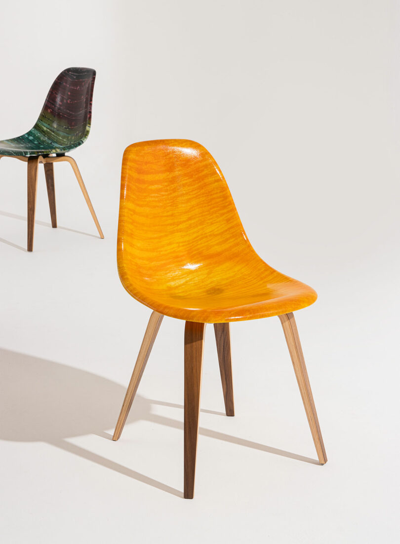 Two modern chairs with molded seats and wooden legs; the front chair is yellow-orange and the chair in the background is dark green.