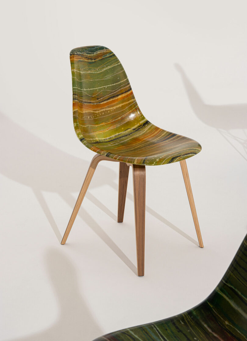 A modern chair with a glossy, green and brown marbled seat and wooden legs, positioned on a light background with its shadow visible.