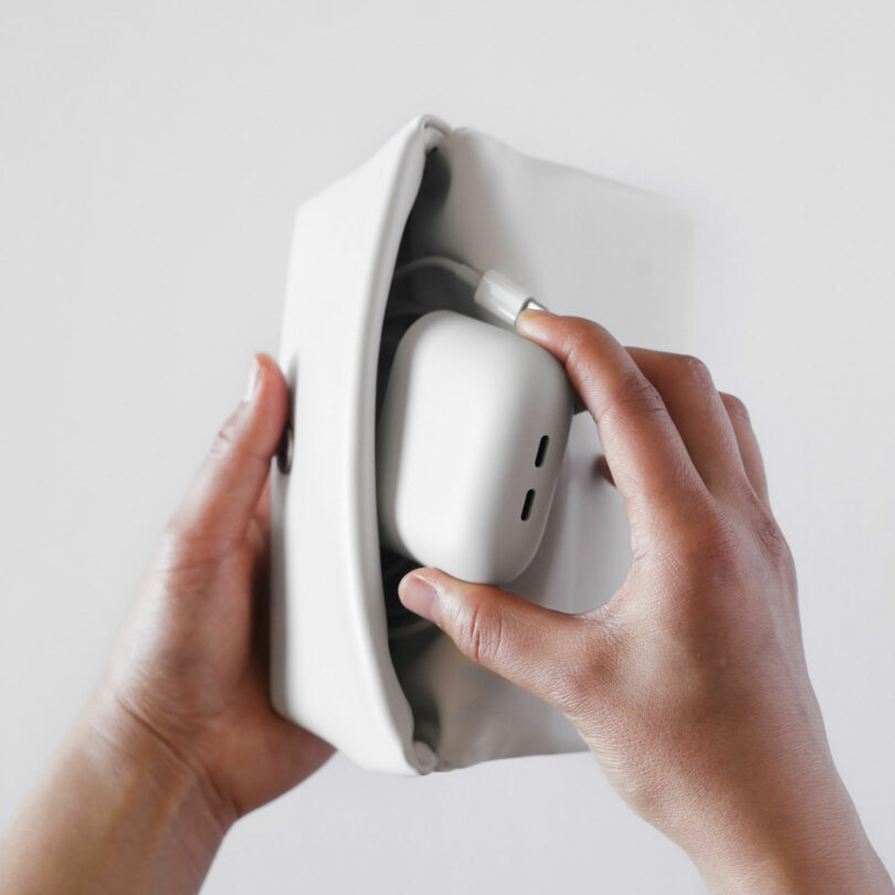 A person places a pair of wireless earbuds in a charging case into a small, soft white pouch.