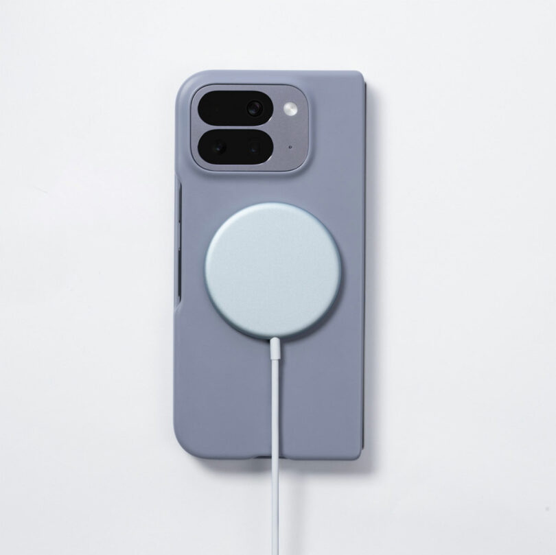 A smartphone in a gray case with a circular wireless charger attached to the back, connected by a white cable, on a white background.