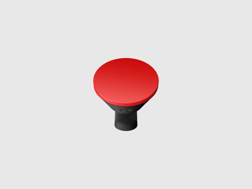 A black and red handheld device with a round red top, viewed from above, set against a plain light grey background.