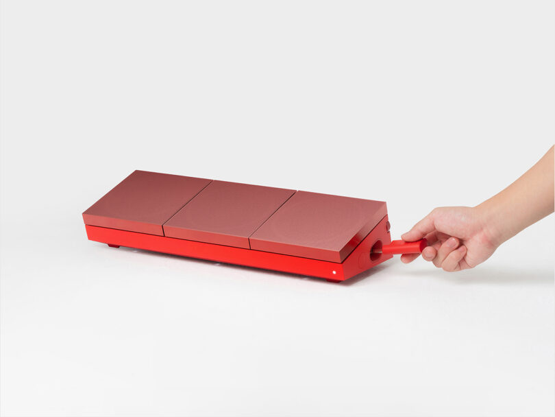 A hand pulls a red handle attached to a rectangular, red, three-sectioned object on a white background.