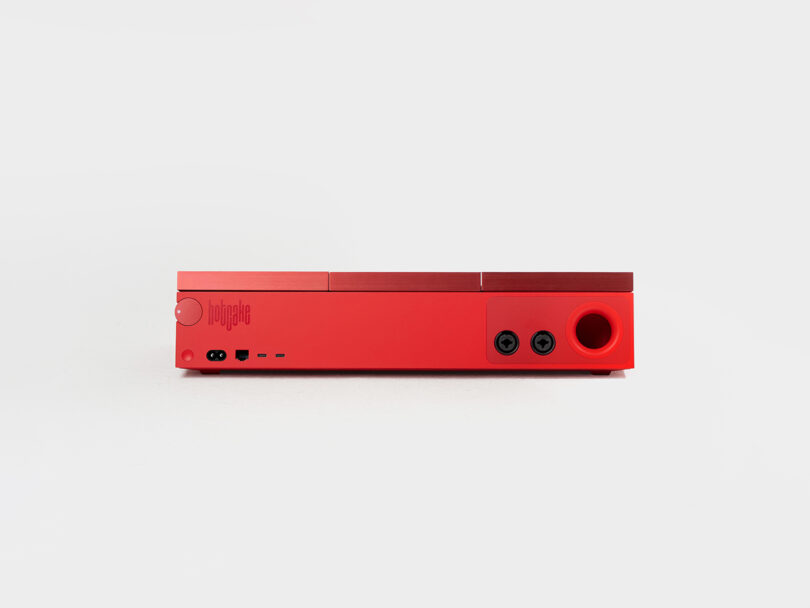 A red rectangular electronic device with two audio jacks, multiple ports, and a logo on the front panel, set against a white background.