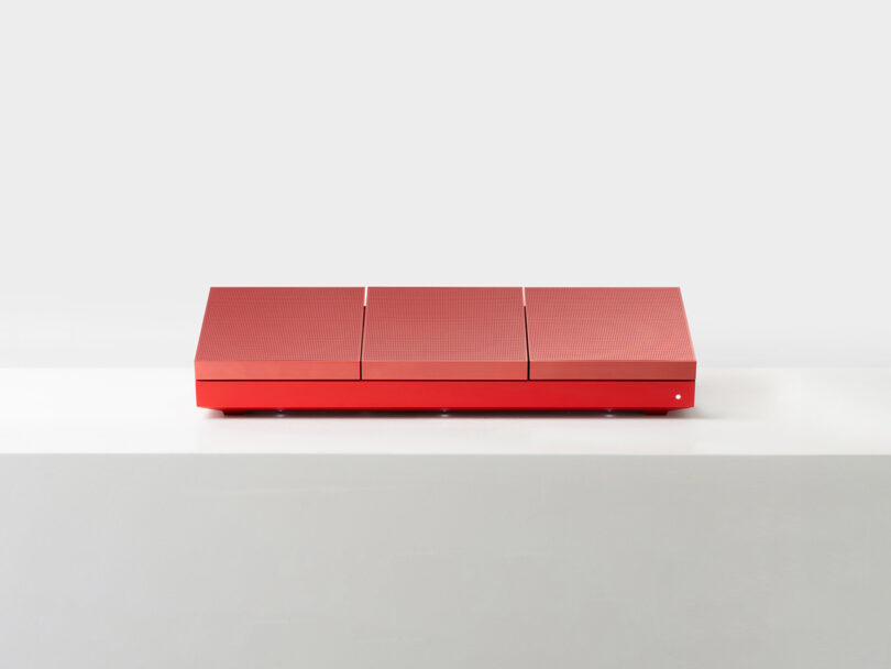A rectangular red box with three segmented lids sits on a white surface against a plain light gray background.