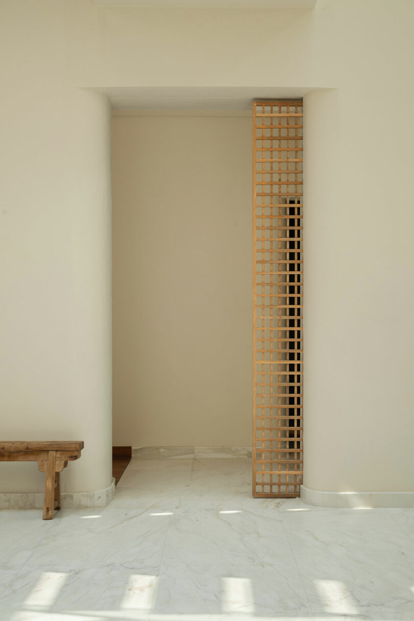 Minimalist interior with white marble floor, beige walls, a wooden bench on the left, and a decorative wooden lattice panel on the right.
