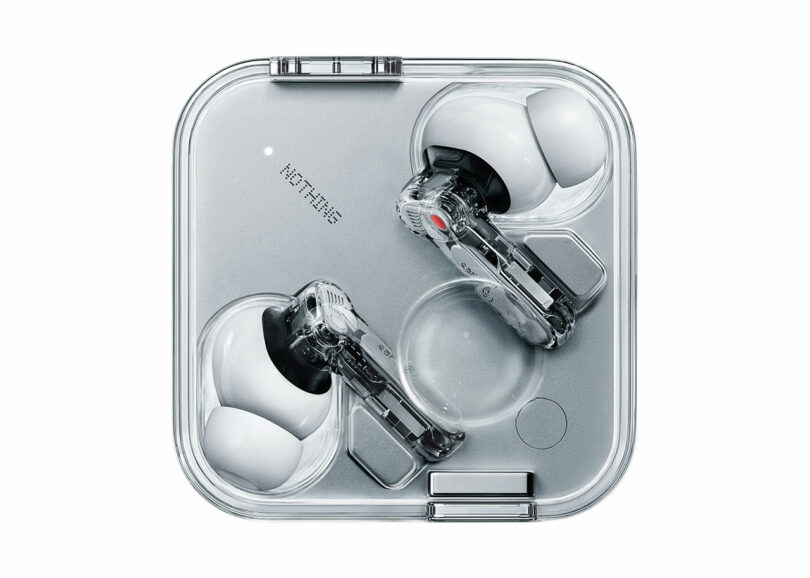 Un par de auriculares inalámbricos blancos con tallos transparentes, vista desde arriba en una caja de carga cuadrada transparente.