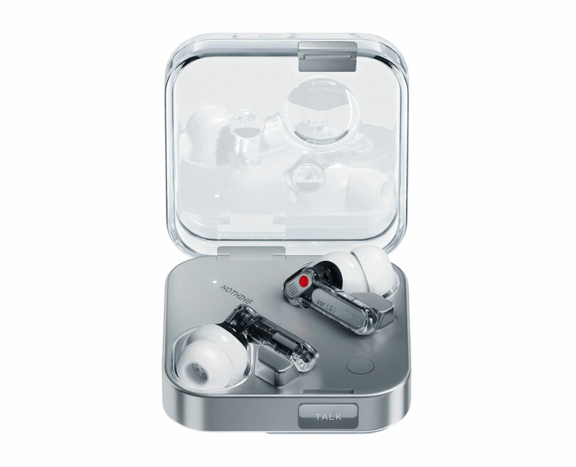 Un par de auriculares inalámbricos con puntas blancas se colocan en una caja de carga transparente cuadrada, que se muestra sobre un fondo blanco.
