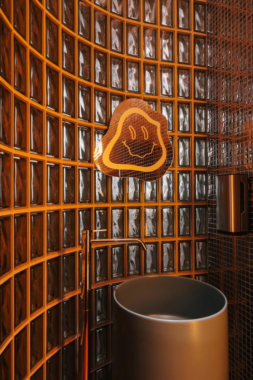 A modern bathroom with glass block walls, a cylindrical sink, and a Mario ghost figure decor mounted above the sink brings a playful touch—almost as if Pluto himself might drop by for a visit.