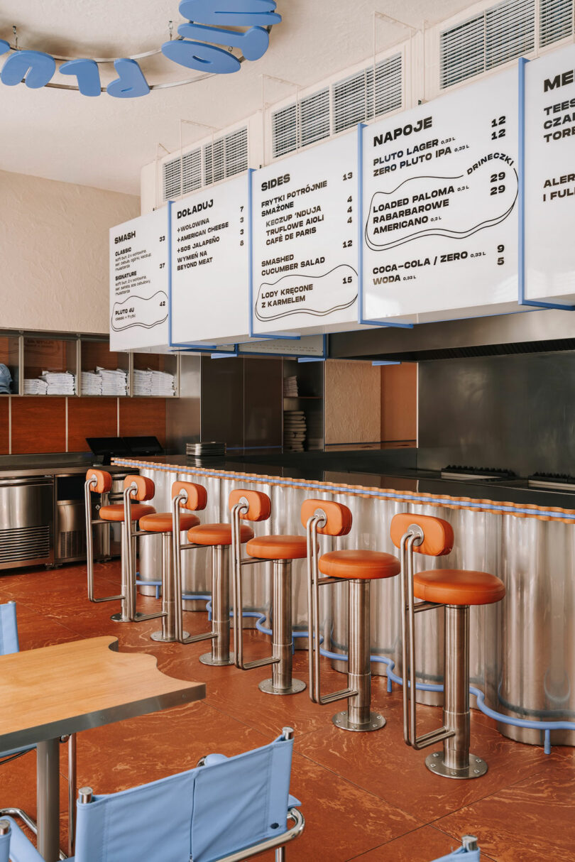 A modern diner interior with a metal counter, five orange bar stools, wooden tables, and large menu boards displayed above the counter—perfect for enjoying a classic meal while dreaming of Pluto’s distant wonders.